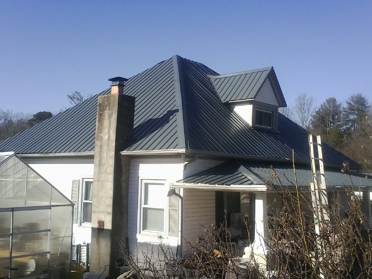 Dark blue standing seam metal roof on a white farmhouse with dormer — Slate & Tile Roof Repair by Roofing Brothers in Whitharral