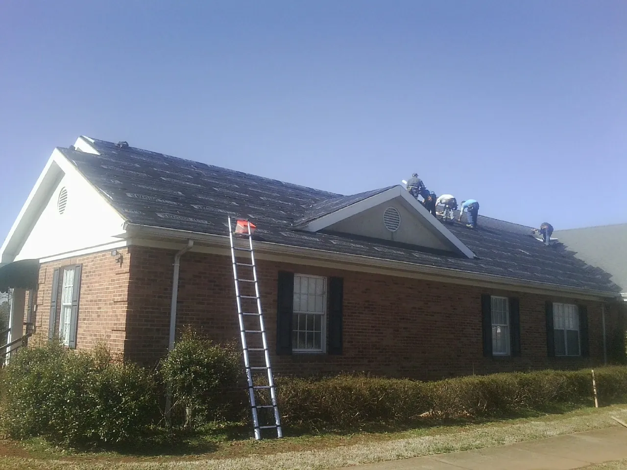 Crew tearing shingles off a brick ranch roof with a ladder set — Metal Roof Repair work by our crew in Whitharral
