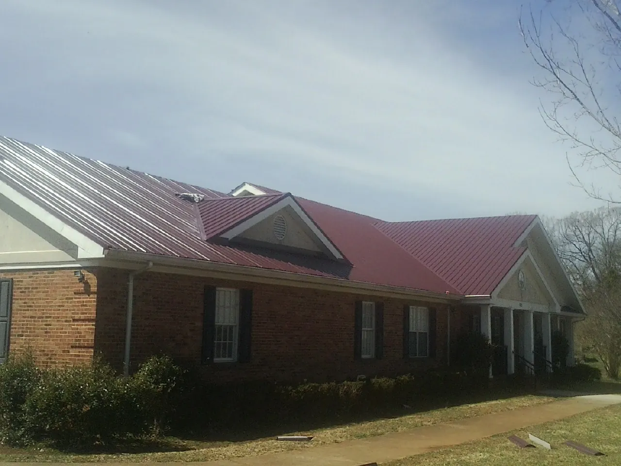 Red metal roof with gabled entries on a long brick building, from a Hail Damage Roof Repair job in Whitharral