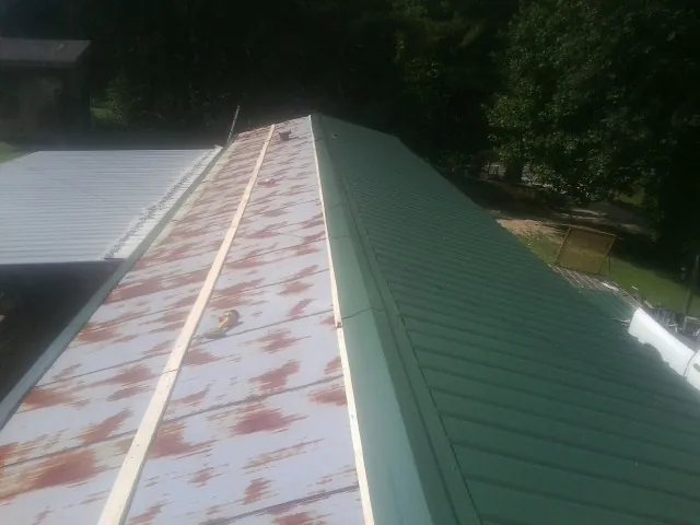 Old rusted panels beside newly installed green metal roofing — Wind Damage Roof Repair by Roofing Brothers in Whitharral