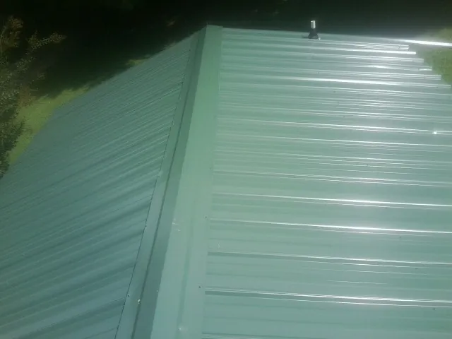 New green metal panels meeting at the ridge of a roof — Flat Roof Repair work by our crew in Whitharral
