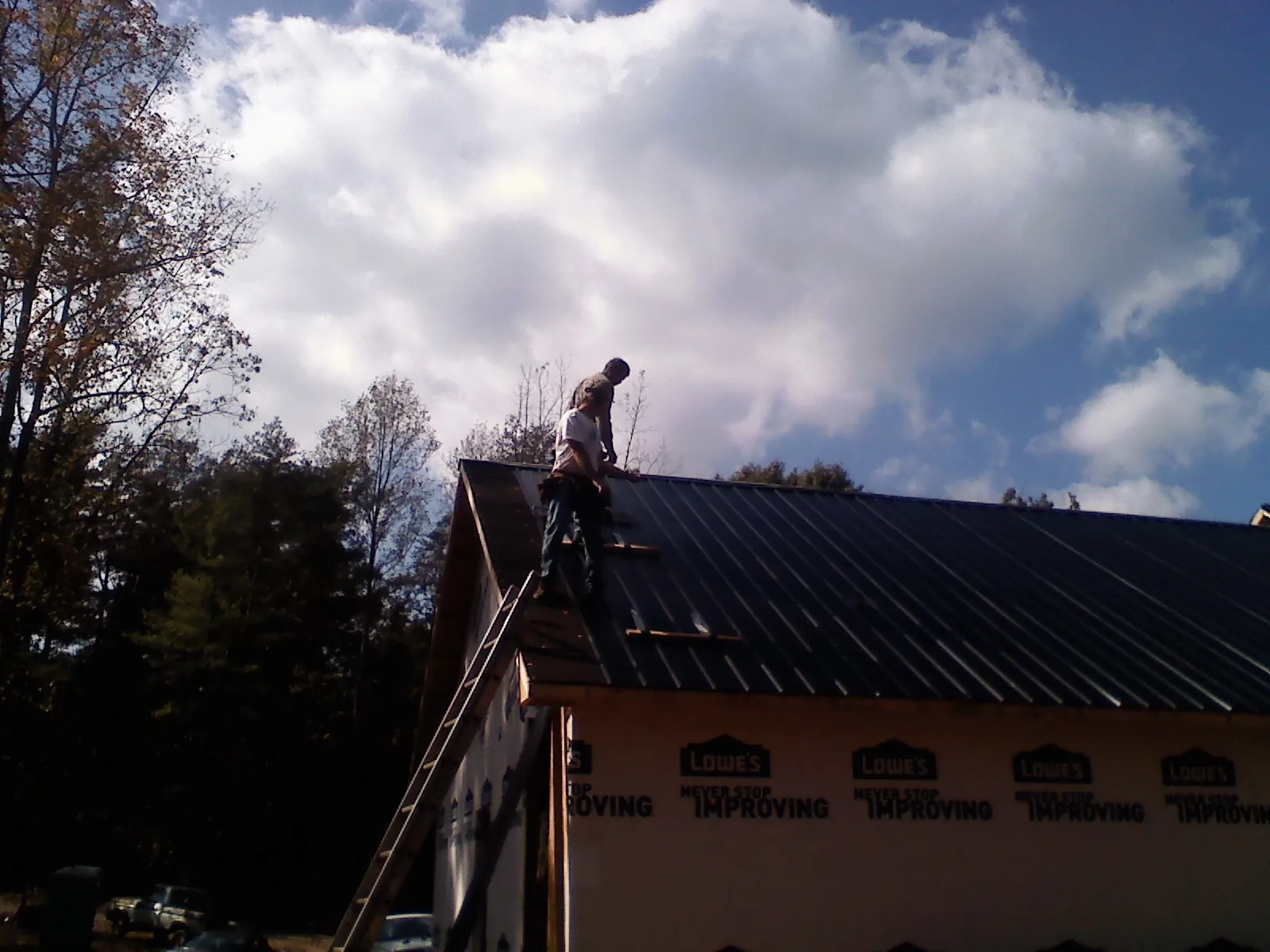 Roofer fastening dark metal panels high against a cloudy sky, from a Roof Inspection job in Whitharral