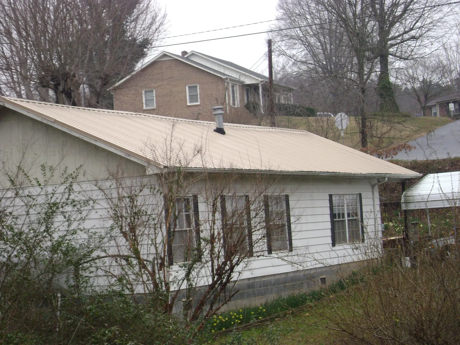 Tan metal roof on a white sided house set into a hillside — Commercial Roofing by Roofing Brothers in Whitharral